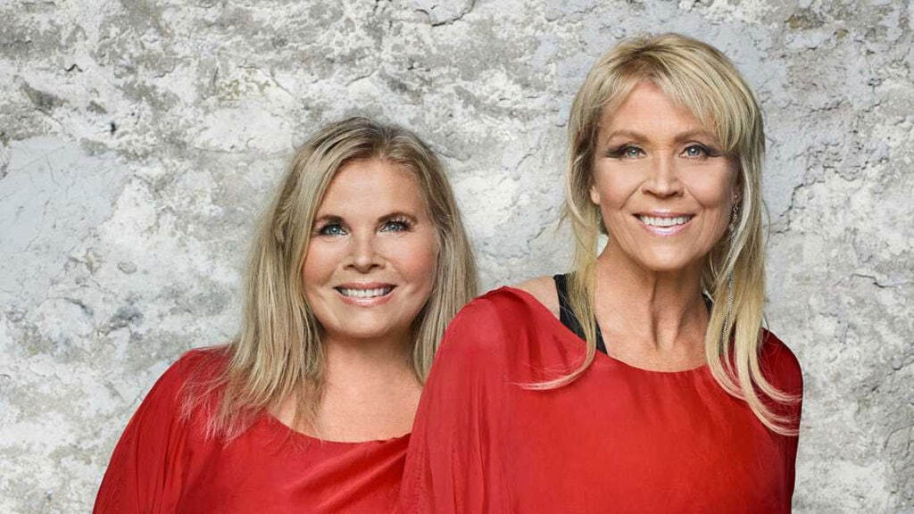 Porträtt på de båda systrarna bredvid varandra. De är klädda i liknande röda och ler brett.