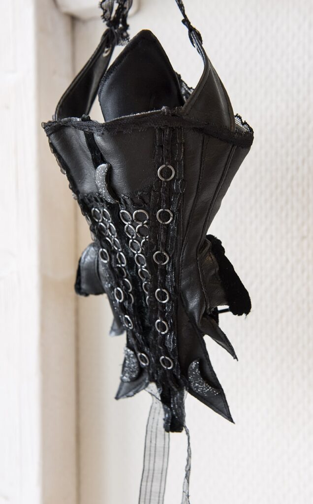 Snörliv med inspiration från 1600-1700-talets mode. Tillverkad av svart läder och med många små metallringar fastsydda i rader uppifrån och ner.