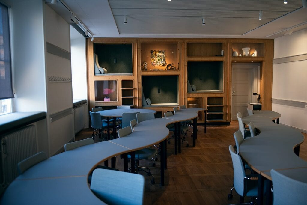 Ett rum med bord i böljande former. Mot väggen som tre inbyggda fyrkantiga nischer i olika höjd där man kan sätta sig. 