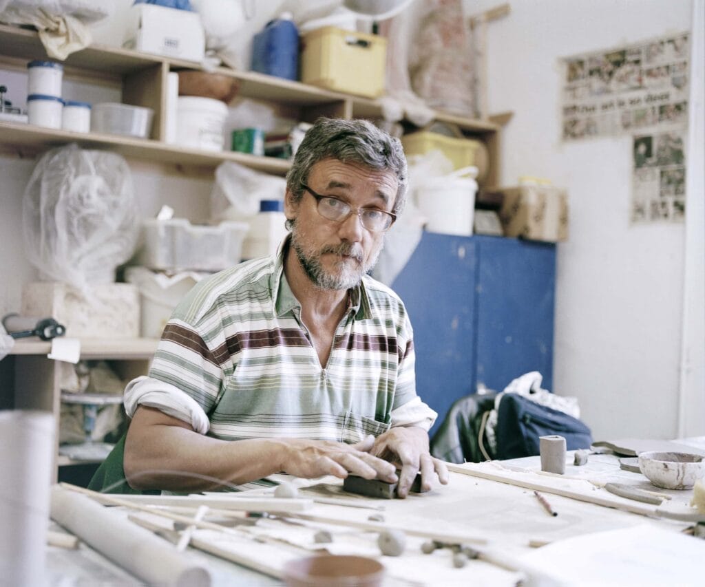 Porträtt på Cameron Morgan där han sitter vid ett bord och arbetar med lera. Cameron är en äldre ljushyad man med glasögon.