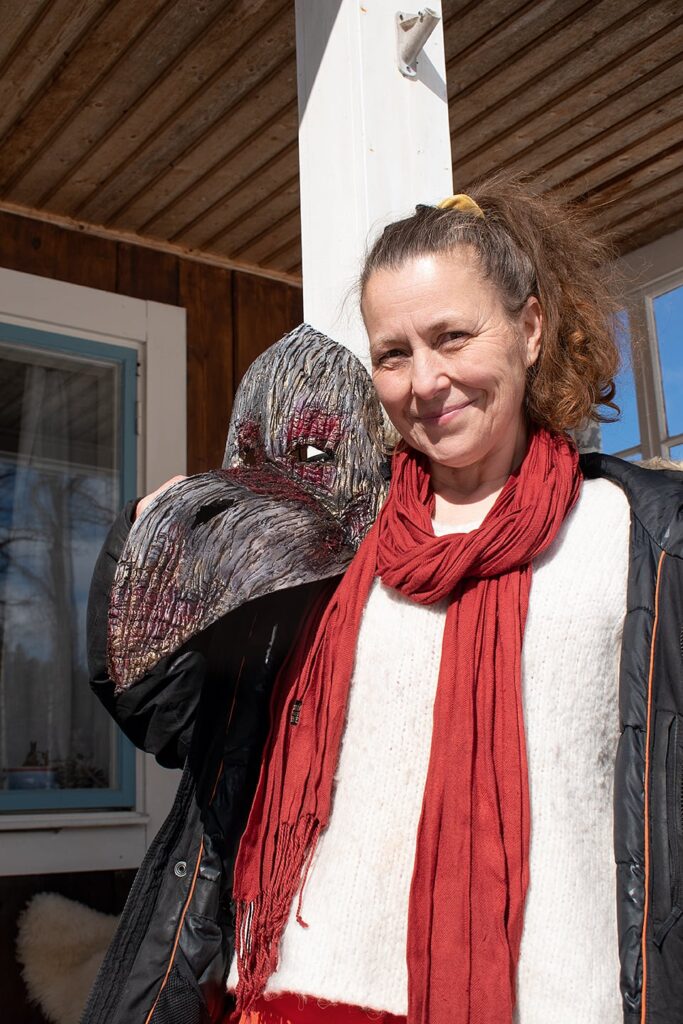 Porträtt på Anna som står utomhus med en slags kråk-mask på axeln.