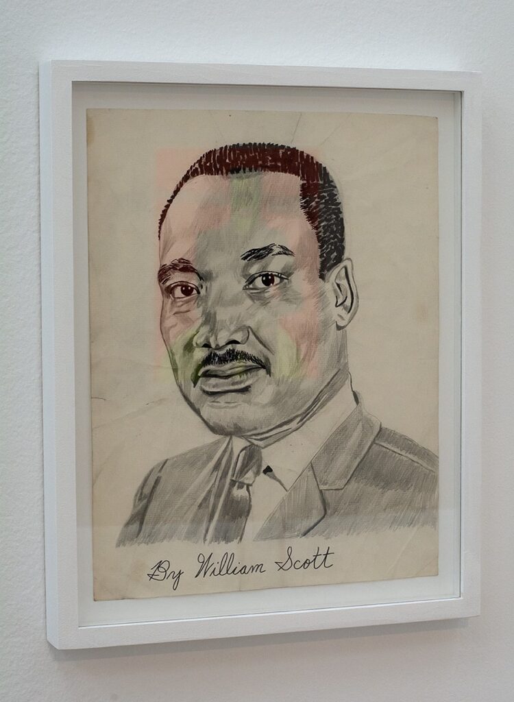 Blyerts på papper. Ett porträtt av Martin Luther King. Målad på beige papper med vit rak träram.