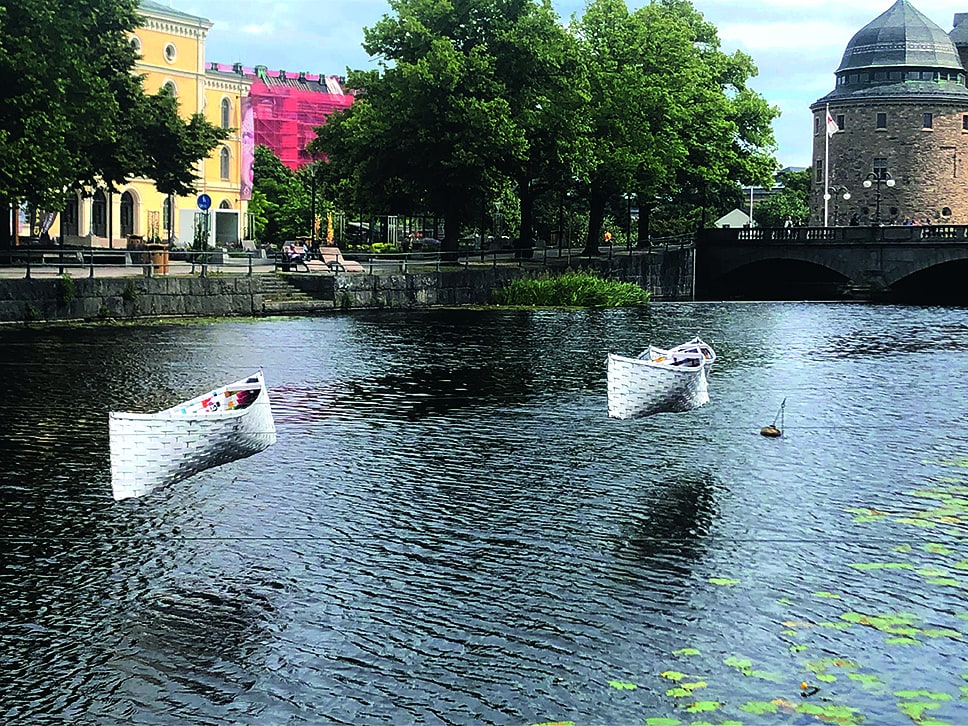 Konstverket består av ett flertal vita flätade båtar som hänger i spända vajrar över en å i staden.