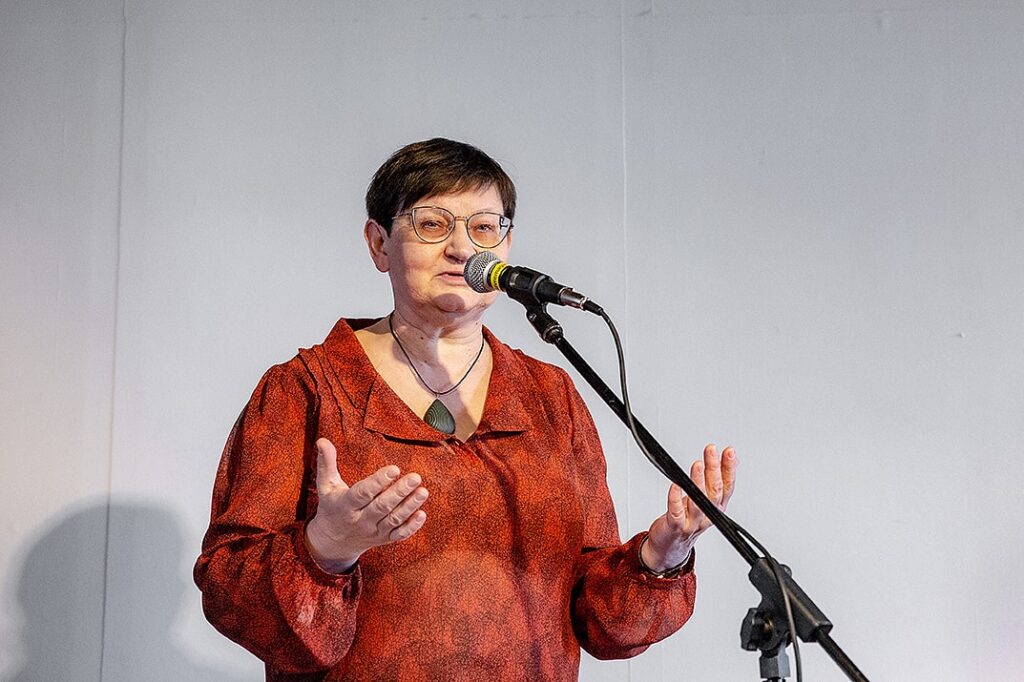 Tamara Sushko står framför ett mikrofonstativ och pratar med öppna händer i en välkomnande gest.