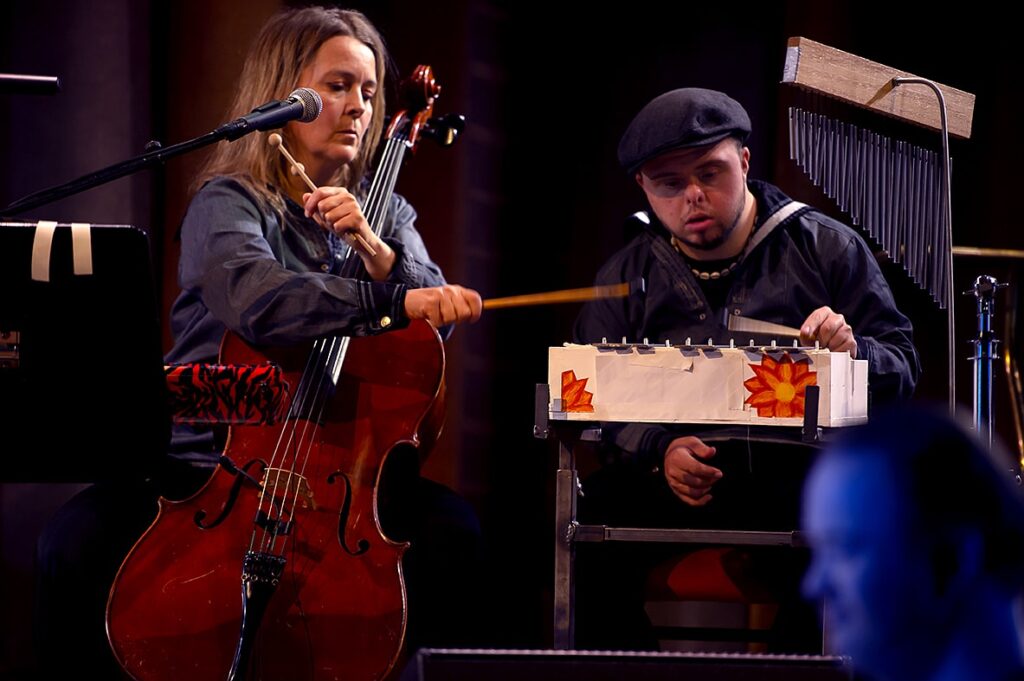 Scenbild med en kvinna sitter med en cello i famnen och en ung man med Downs syndrom sitter böjd över en liten xylofon.