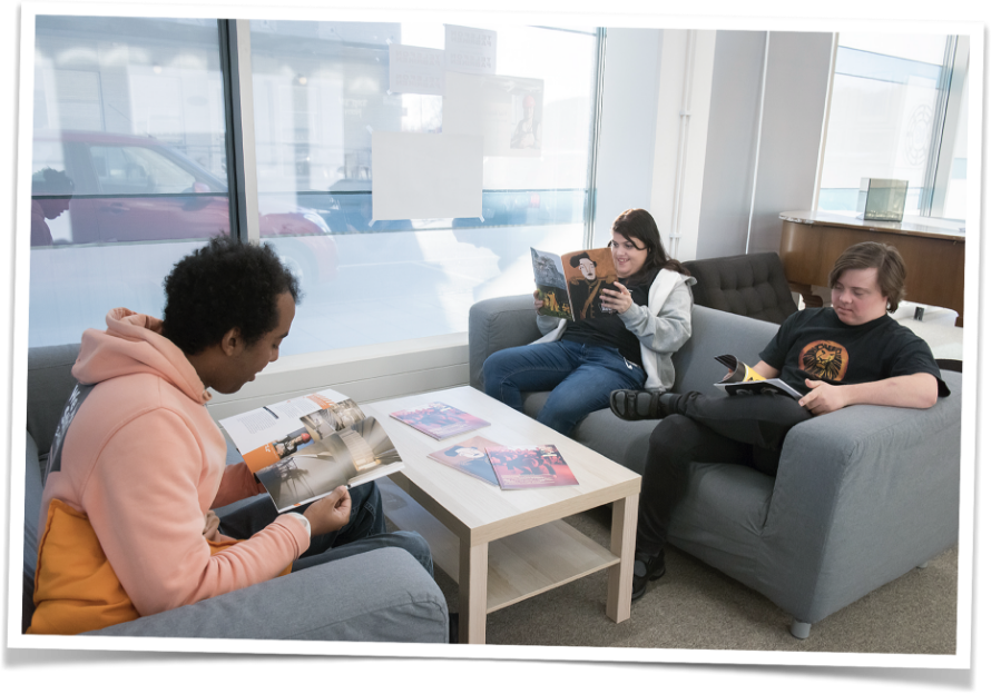 tre personer sitter i en soffa och läser magasinet