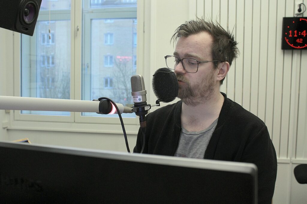 Överkroppsbild på Jonas som står i studio och pratar i en mikrofon.