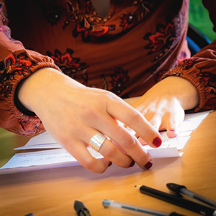 Närbild på händer som arrangerar pappersremsor med skrivna meningar på ett bord.