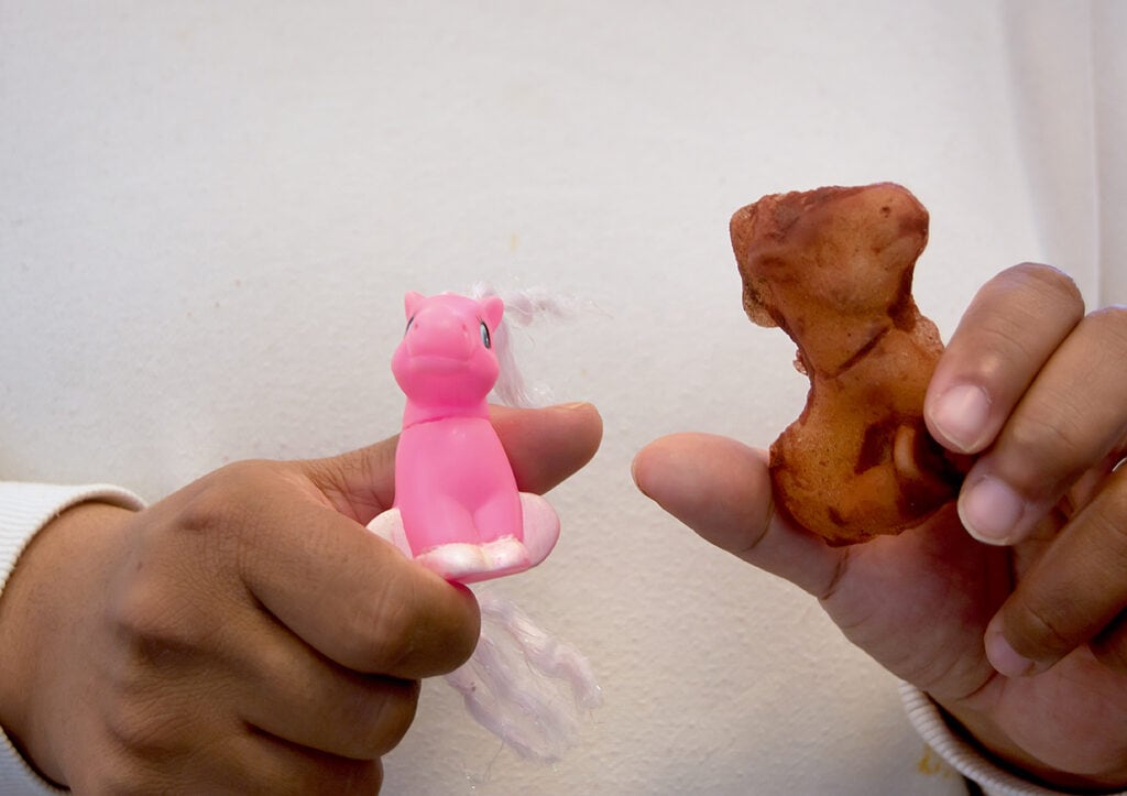 Närbild på två händer som håller fram två figurer. Den ena en liten till vänster leksakshäst och en brun modellerad form av leksakshästen till höger.