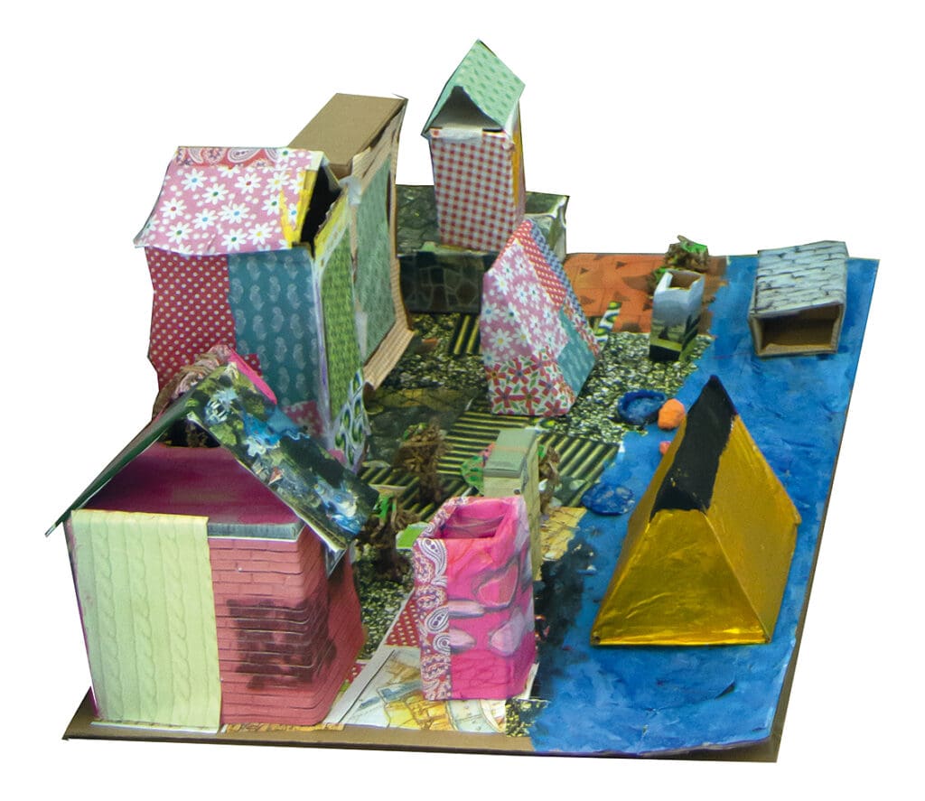 En fantasifull modellstad i minityr uppbyggd i vad som verkar vara kartong och inklädd i brokiga och färgglada textiler på en fyrkantig kartongyta.