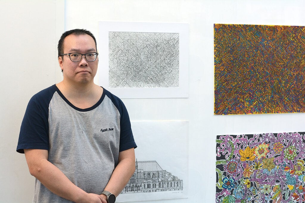 David Cheung står framför en vägg där några av hans konstverk hänger.