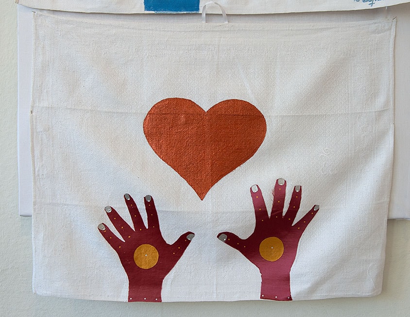 En vit kökshandduk och ett rött målat hjärta i mitten och två brunröda händer som sträcker sig mot hjärtat.