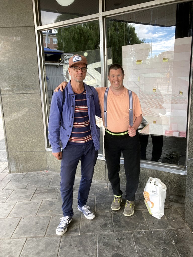 Toffe och konstnärskollegan Jan-Albert Carlsson står bredvid varandra på en grå trottoar. Toffe håller armen om sin vän, med handen vilande på Jan-Alberts axel. 